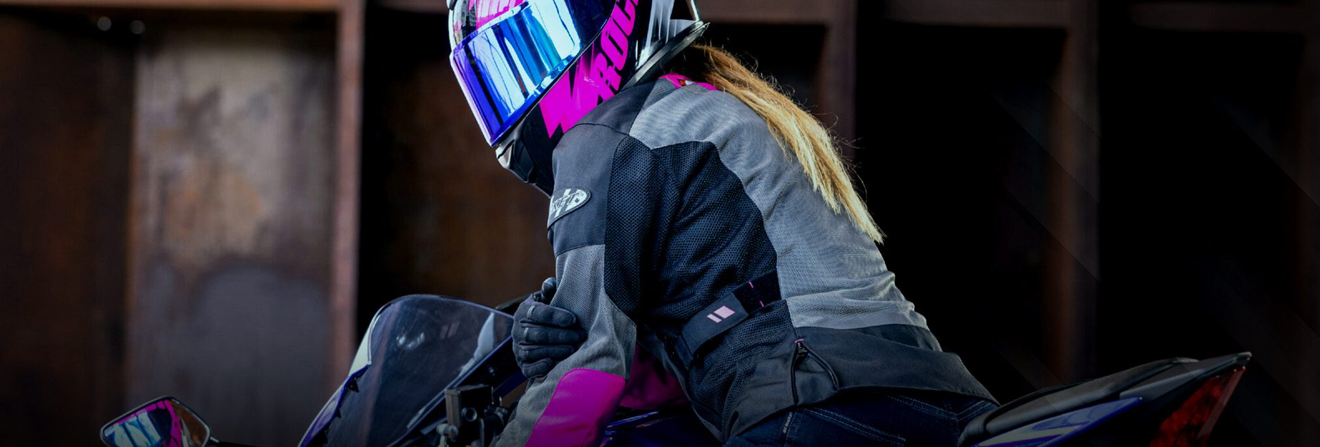 Motociclista mujer con casco integral rosa y chamarra de protección Joe Rocket, lista para rodar en moto deportiva.