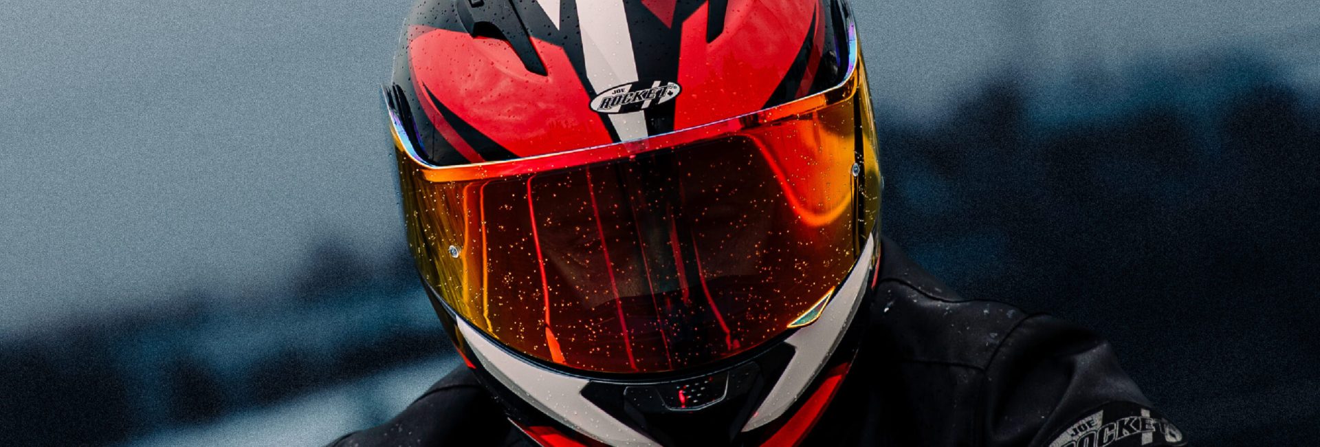 Motociclista con casco abatible rojo Joe Rocket y chamarra impermeable, bajo la lluvia.