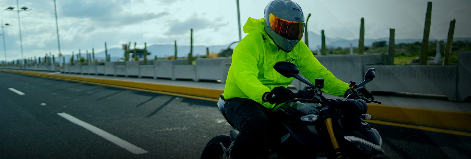 Motociclista con impermeable fosforescente Joe Rocket y casco integral, rodando en carretera sobre motocicleta naked.